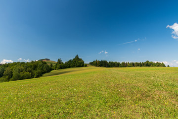 beautiful mountain scenery with hills covered by mix of meadows and forest and blue sky with only few clouds