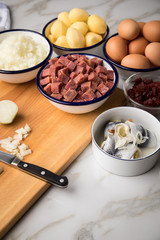 Zutaten  für Norddeutscher Hamburger Labskaus mit Rindfleisch Corned Beef, Rote Beete, Kartoffeln, Saure Gurken, Zwiebeln, Ei und Rollmops auf Marmor Arbeitsfläche