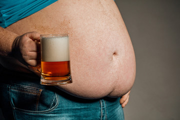 A man with a fat belly holding a glass of beer. On dark background.