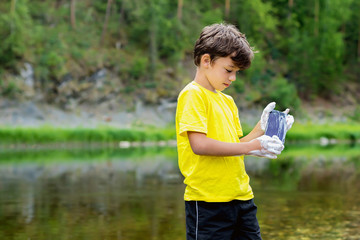 A schoolboy in a yellow t-shirt and black shorts is standing near the river in nature, holding a...