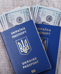 Ukraine biometric passport and cash US dollars, on a light wooden background.