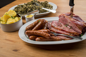 Kassler Nacken, Kohlwurst, Pinkel und Oldenburger Grünkohl auf Platten mit Kartoffeln und Senf auf Holz Tisch