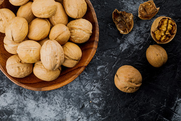 plate with some raw walnuts and peel on dark background