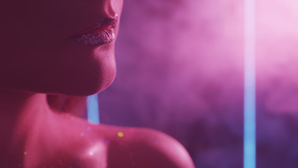 Color smoke face. Night glam. Woman with glitter lips bare shoulder in purple neon light.