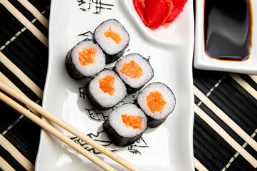 rolls with red fish on a white plate. Chinese chopsticks. Soy sauce in a white cup.