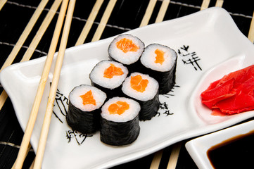 rolls with red fish on a white plate. Chinese chopsticks. Soy sauce in a white cup.