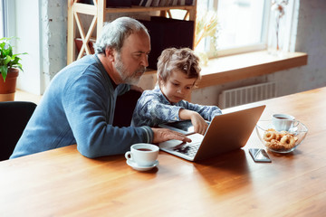Using devices. Grandfather and his grandson spending time together insulated at home. Having fun, stadying online, reading and cleaning up. Concept of quarantine, family, love, realtions, togetherness