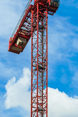 Red tower crane against blue sky with white clouds. Close up. Front shot. Copy space.