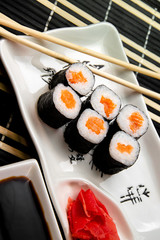 rolls with red fish on a white plate. Chinese chopsticks. Soy sauce in a white cup.