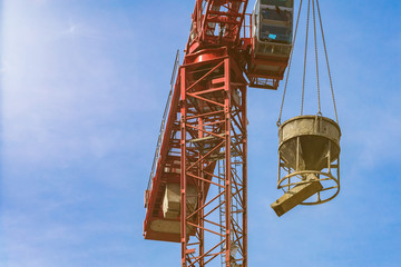 Red tower crane with cement mixer against blue sky with white clouds. Close up. Front shot. Glare of the sun on the cabin builder. backdrop