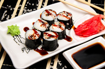 Roll with eel on a white plate. Red ginger Soy sauce in a white cup. Chinese chopsticks
