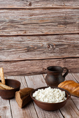 Fresh cottage cheese in a wooden bowl with a spoon, jar of sour cream on a wooden old background. Rich in Protein and Calcium healthy dairy product, low fat soft white cheese. With bread and hay.