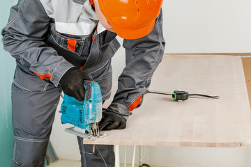 A male Builder cuts a wooden beam with an electric jigsaw, male hands with an electric jigsaw. Working with a tree.