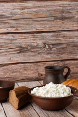 Fresh cottage cheese in a wooden bowl with a spoon, jar of sour cream on a wooden old background. Rich in Protein and Calcium healthy dairy product, low fat soft white cheese. With bread and hay.