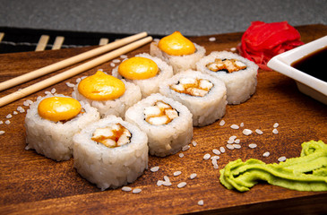 Orange rolls with chicken on a wooden board. Chinese chopsticks. Soy sauce in a white cup.