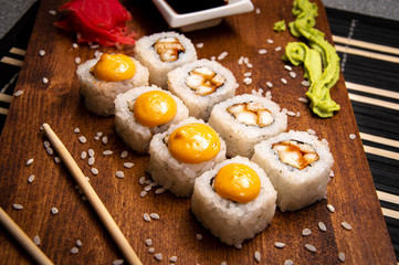 Orange rolls with chicken on a wooden board. Chinese chopsticks. Soy sauce in a white cup.