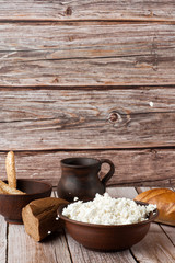Fresh cottage cheese in a wooden bowl with a spoon, jar of sour cream on a wooden old background. Rich in Protein and Calcium healthy dairy product, low fat soft white cheese. With bread and hay.