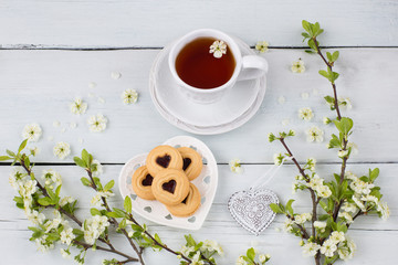 tea in a cup, cookies and cherry branches on the table