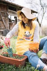 Obraz premium Female gardener holding hand shovel and pot while sitting on ground