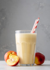 Fresh protein shake with nectarine or peach on a white wooden table. Fresh apricot milkshake. A glass of peach smoothie.
