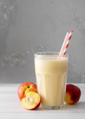 Fresh protein shake with nectarine or peach on a white wooden table. Fresh apricot milkshake. A glass of peach smoothie.