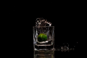 Water splashing out from a glass due to the immersion of a fresh green small lime into it.