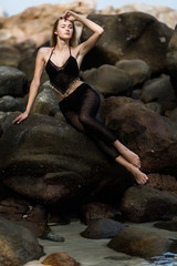 Young pretty woman in black bikini sitting on the cliff near Sea