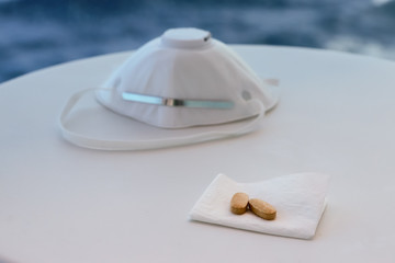 Protective mask N95 respirator and pills on white table on a sea background. COVID-19 concept.