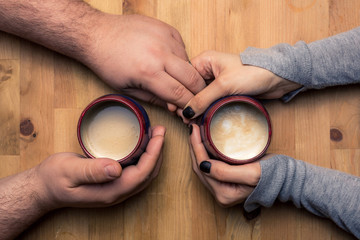 Man and woman holding hands with coffee lattes on a wooden table