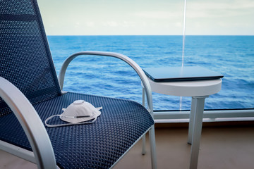 Mask n95 respirator on the chair and laptop on white table on a cruise ship balcony on sea background.