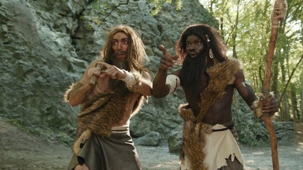 Prehistoric wild tribesmen hunting for food searching animals in green forest rocks landscape. Nomadic african barbarians on hunting. Hunter-gatherers. Homo sapiens.