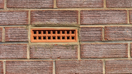 Terracotta coloured air brick embedded with a textured red brick wall.