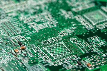 Macro image of a green computer printed circuit board with empty spaces for unsoldered elements and selective focus