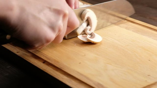 Hands of a woman cutting mushrooms on a wooden Board. Close up