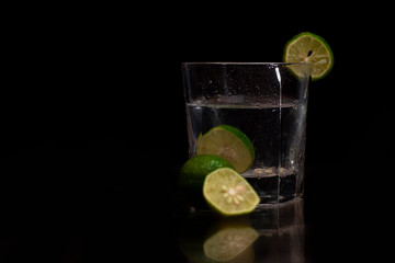 Water splashes out of the garnished glass as a green fresh lemon slice immerses into the water.