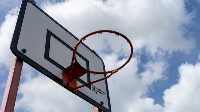 Outdoor Basketball hoop with white wooden backboard, black indication strips and faded red metal hoop and legs.