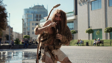 Primitive bowman of hunter-gatherers walking in slow motion exploring city of today. Neanderthal...