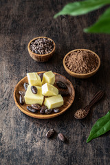 Cacao products  - butter, powder, whole beans, nibs, original leaves on old rustic background.