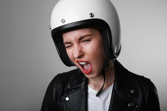 Headshot of young woman wearing a motorcycle helmet over isolated background making funny face. Free space for text.
