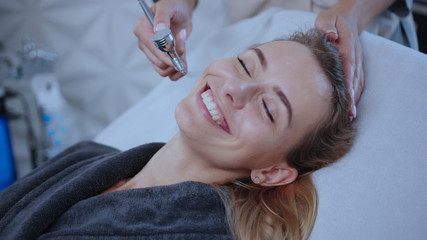 Obraz na płótnie Canvas Happy smiling young woman in beauty salon enjoying skincare mesotherapy medical facial massage on spa procedure. Professional hardware cosmetology.