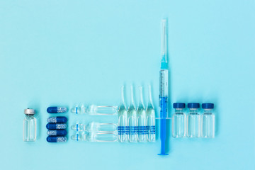 Thermometer, pills, injection ampoules, syringe for vaccination on a blue background, healthcare...
