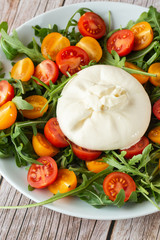 Tasty, fresh salad with mozzarella burrata, arugula, cherry tomatoes and basil on a white plate on a wooden background.Close up. Healthy Italian food. Selective focus