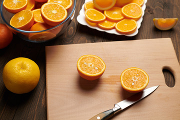 Fresh orange fruit whole and sliced on a wooden table, cutting board and kitchen knife. A plate full of citrus slices - natural and healthy food. Glass of fruit cocktail.