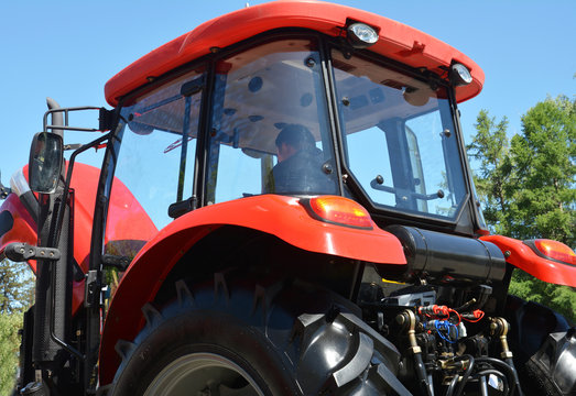 Rear view of a new red tractor glass cabin with rear lights, indicators and a driver inside.