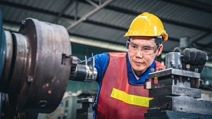 Portrait of a young Asian industrial worker using measuring tool on the machine.