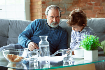 Coffee drinking. Grandfather and his grandson spending time together insulated at home. Having fun, reading magazine, happy. Concept of quarantine, family, love, realtions, togetherness, education.