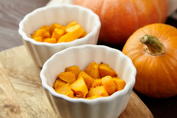 Pieces of baked pumpkin in white ceramic bowl on wooden background