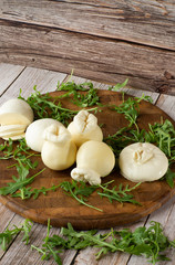 Italian cheese burrata on a wooden table close up. Mini whole tied Italian cheese burrata on small wooden cutting board served with arugula over wooden texture background. Overhead view.