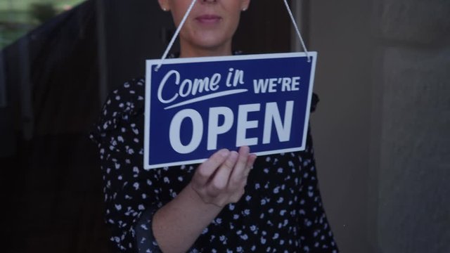 4K: Woman turning over Open / Closed sign in shop window. Stock Video Clip Footage. Opening up