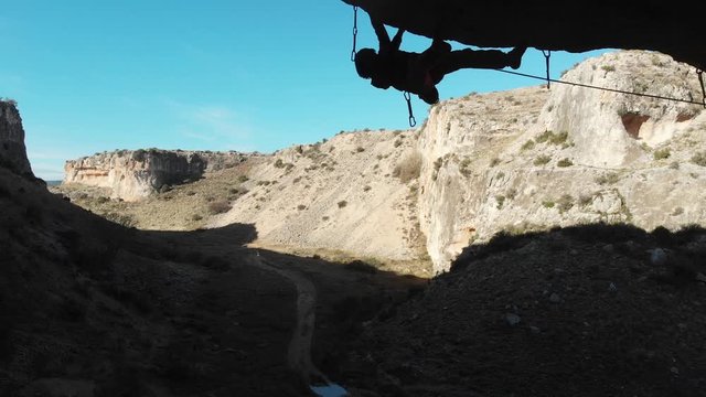The man climbs onto the roof secured with a rope. Aerial view. Zafran&eacute; Valley, the town of Alborton. Zaragoza, Spain. Climbing concept.4K.Drone